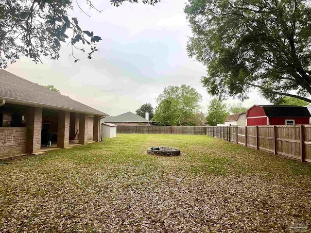 view of yard featuring an outdoor fire pit, a fenced backyard, an outdoor structure, and a storage shed
