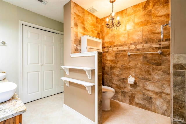 bathroom with tile walls, vanity, toilet, a chandelier, and tile patterned floors