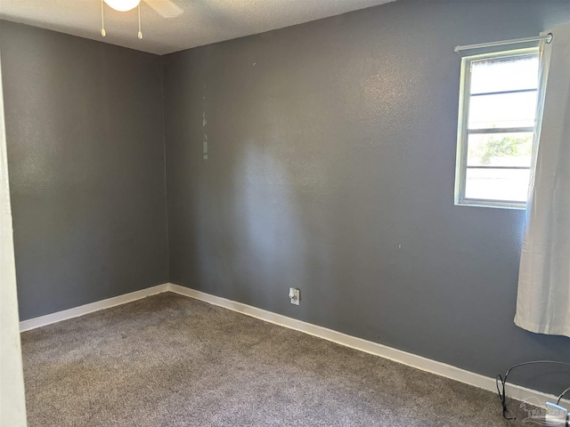 empty room with a ceiling fan, baseboards, dark colored carpet, and a textured ceiling