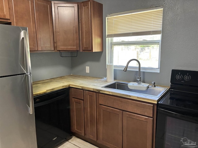 kitchen featuring brown cabinetry, butcher block counters, black appliances, and a sink