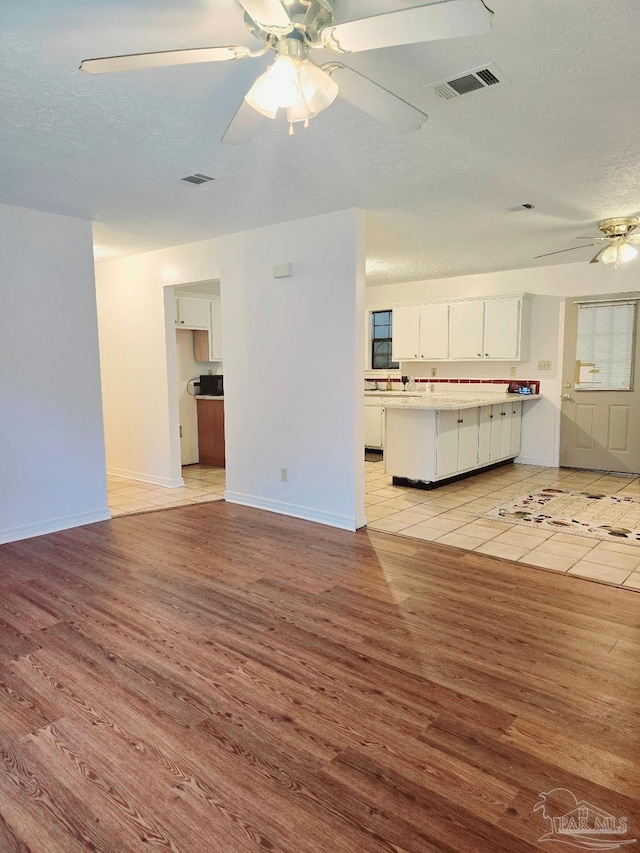 unfurnished living room with ceiling fan, light hardwood / wood-style floors, and a textured ceiling