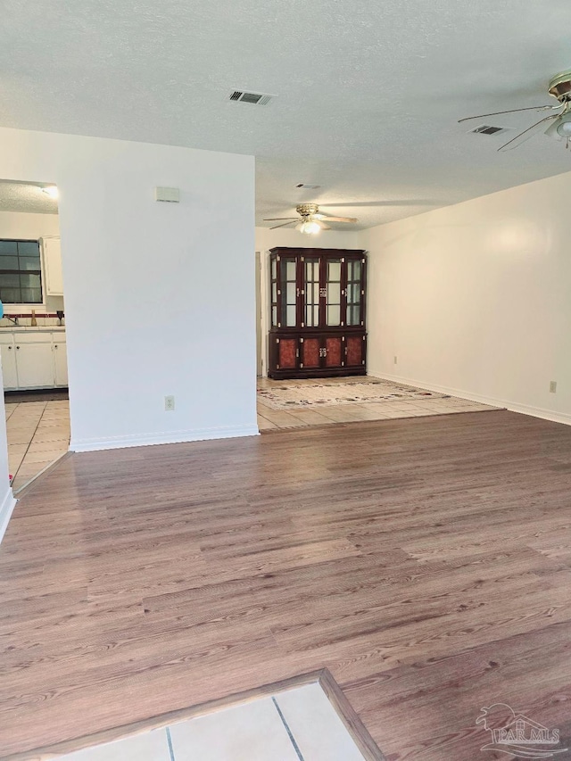 unfurnished living room with a textured ceiling, light hardwood / wood-style flooring, and ceiling fan