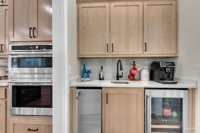 kitchen with double oven, wine cooler, light brown cabinetry, sink, and backsplash