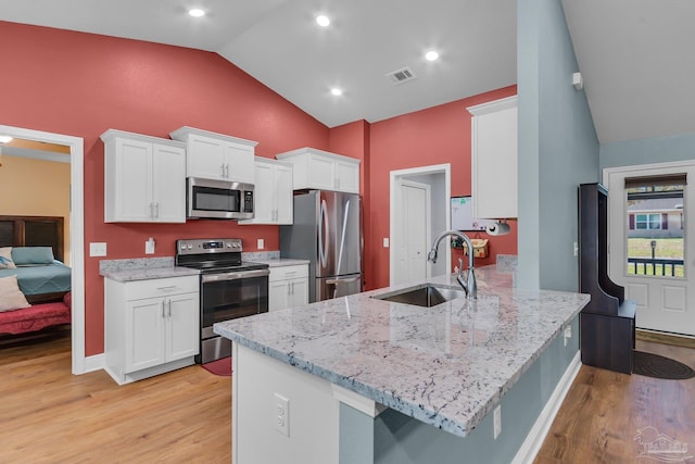 kitchen featuring a sink, appliances with stainless steel finishes, a peninsula, lofted ceiling, and white cabinets