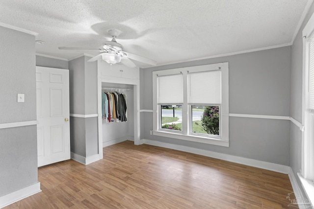 unfurnished bedroom with crown molding, wood finished floors, a closet, a textured ceiling, and a ceiling fan