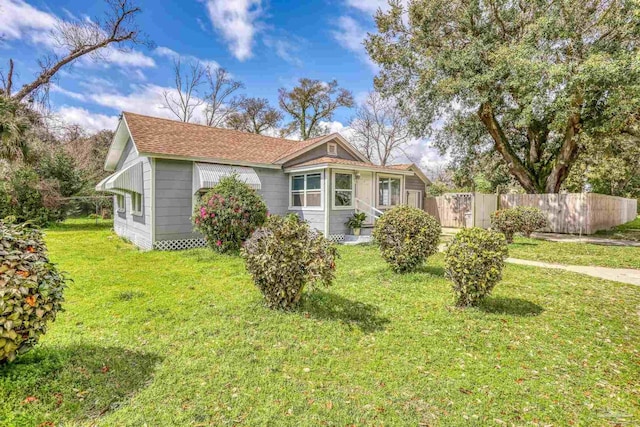 view of front of home with roof with shingles, a front lawn, and fence