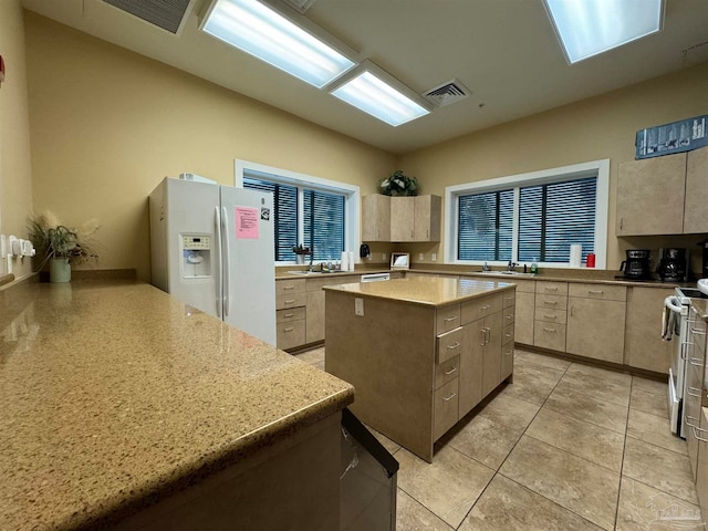 kitchen featuring light brown cabinets, white fridge with ice dispenser, plenty of natural light, a kitchen island, and stainless steel range oven