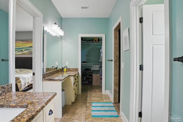 ensuite bathroom with vanity, ensuite bath, a walk in closet, visible vents, and baseboards