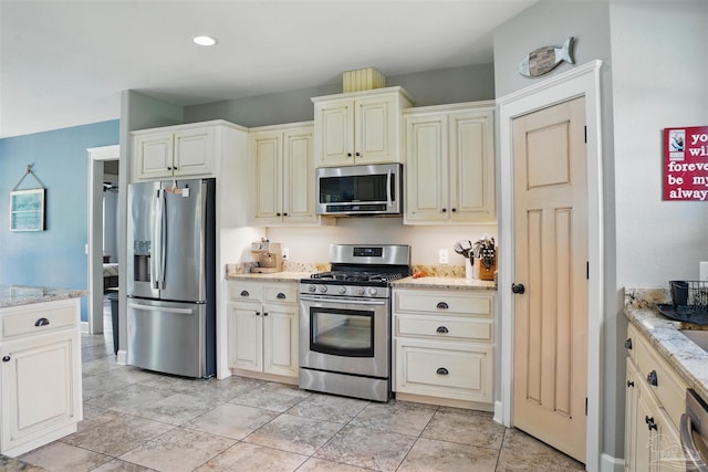 kitchen with cream cabinets, light stone counters, and stainless steel appliances