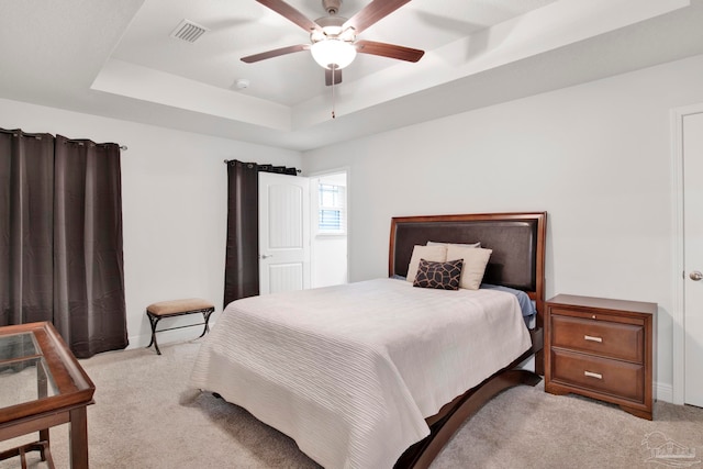 bedroom featuring a tray ceiling, light carpet, and ceiling fan