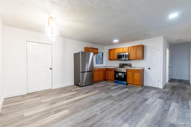 kitchen featuring a textured ceiling, stainless steel appliances, and light hardwood / wood-style flooring