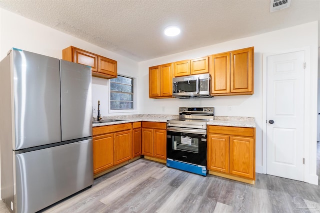 kitchen with a textured ceiling, stainless steel appliances, light hardwood / wood-style flooring, and sink