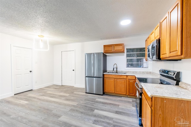 kitchen featuring a textured ceiling, stainless steel appliances, light hardwood / wood-style flooring, and sink