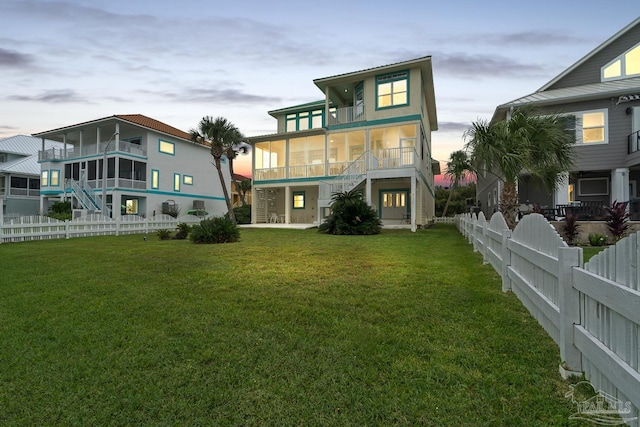 back house at dusk with a lawn and a sunroom