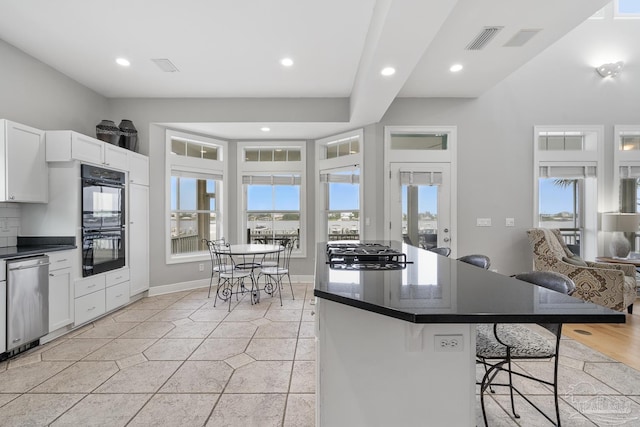 kitchen featuring white cabinetry, a breakfast bar area, decorative backsplash, light tile patterned floors, and appliances with stainless steel finishes