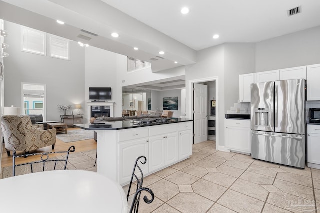 kitchen featuring backsplash, black appliances, kitchen peninsula, a towering ceiling, and white cabinetry