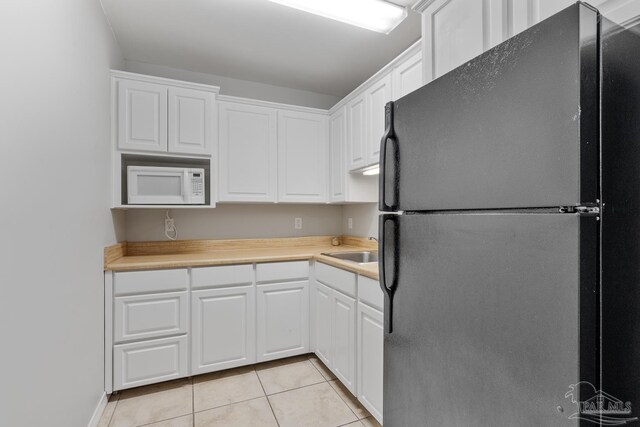 kitchen with white cabinets, black fridge, light tile patterned floors, and sink