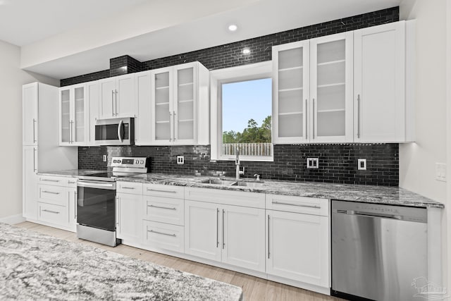 kitchen with sink, tasteful backsplash, light stone counters, white cabinetry, and stainless steel appliances