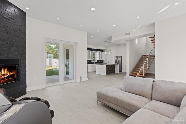 living room featuring french doors, light hardwood / wood-style floors, and a stone fireplace