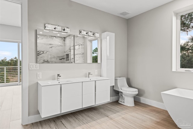 bathroom with a washtub, toilet, wood-type flooring, and vanity