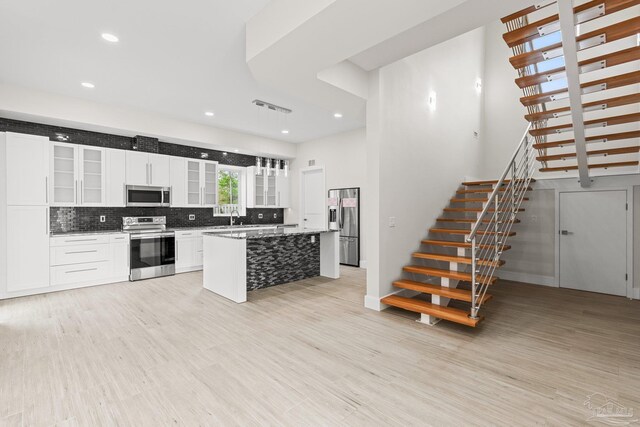 kitchen with light wood-type flooring, tasteful backsplash, stainless steel appliances, a center island, and white cabinetry