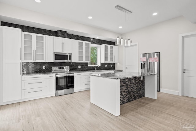 kitchen with dark stone counters, hanging light fixtures, light hardwood / wood-style floors, a kitchen island, and stainless steel appliances