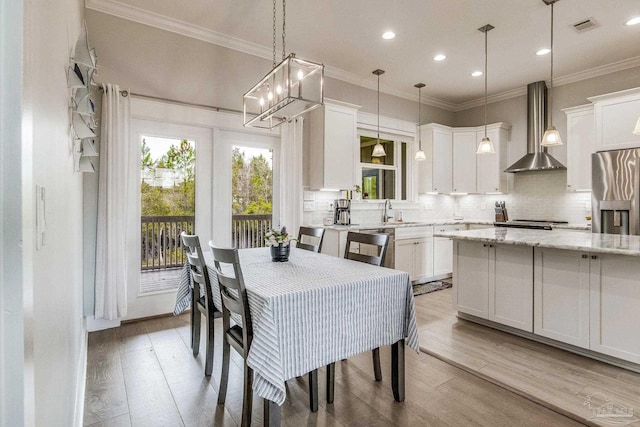 dining space with sink, crown molding, and light hardwood / wood-style floors