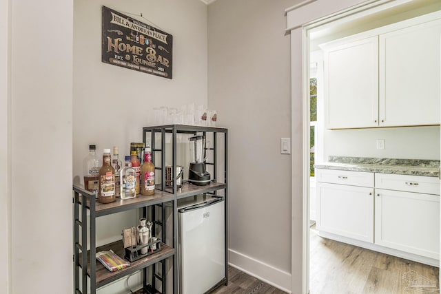 interior space featuring white cabinetry, dark hardwood / wood-style floors, light stone countertops, and stainless steel refrigerator