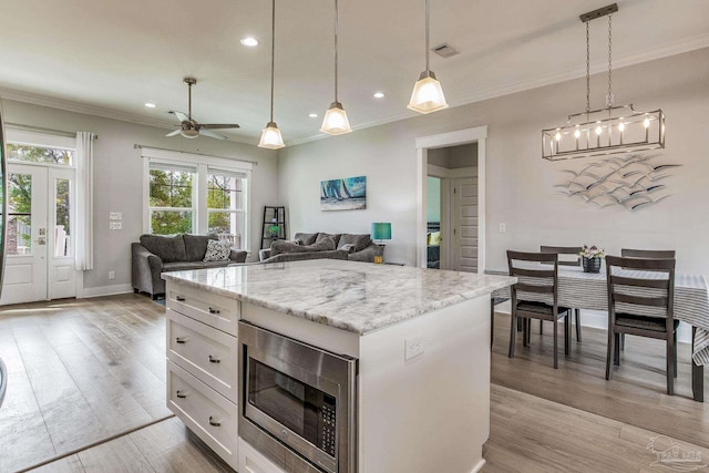 kitchen featuring white cabinetry, decorative light fixtures, light hardwood / wood-style flooring, stainless steel microwave, and a kitchen island