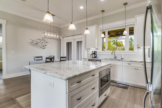 kitchen with sink, white cabinetry, a center island, appliances with stainless steel finishes, and light stone countertops