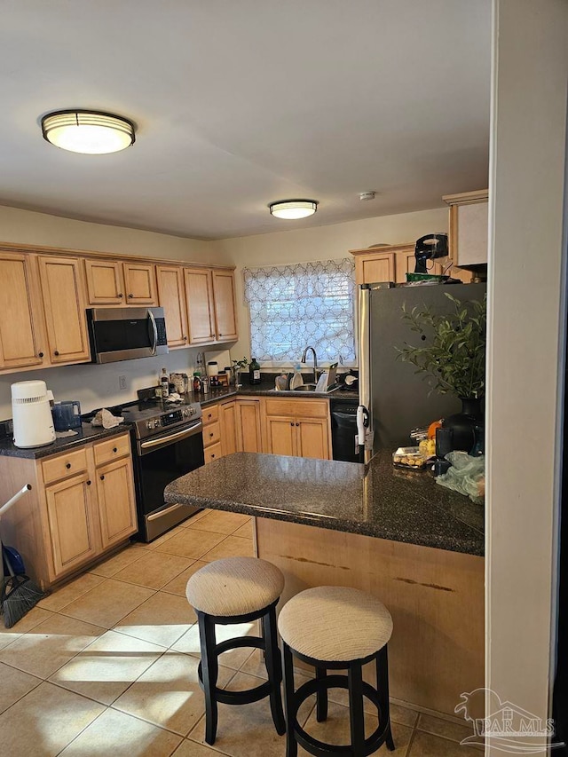 kitchen featuring a sink, a peninsula, appliances with stainless steel finishes, and light brown cabinets