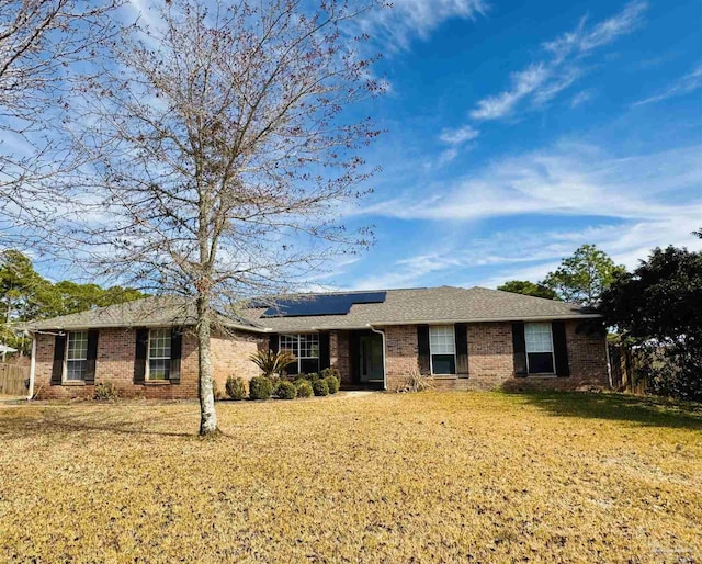 ranch-style home featuring a front yard, brick siding, and solar panels