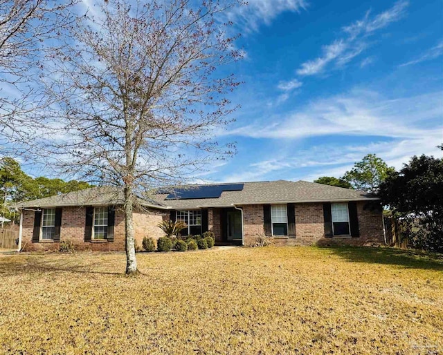 single story home with brick siding, solar panels, and a front lawn