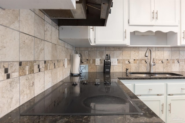 kitchen featuring white cabinets, a sink, dark stone counters, black electric stovetop, and backsplash