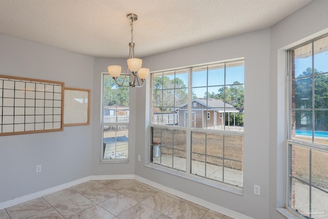 unfurnished dining area featuring baseboards, plenty of natural light, a notable chandelier, and a textured ceiling