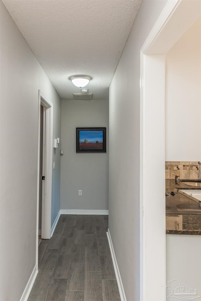 hallway featuring dark wood-style flooring, baseboards, and a textured ceiling
