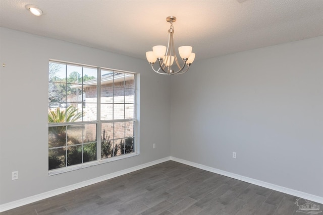 empty room featuring a chandelier, dark wood-type flooring, and baseboards