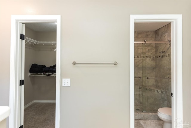 bathroom with a shower stall, a spacious closet, baseboards, and toilet