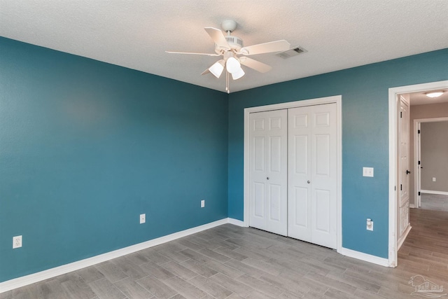 unfurnished bedroom with a textured ceiling, a closet, visible vents, wood finished floors, and baseboards