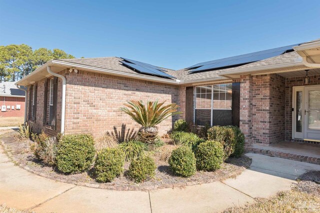 view of side of home featuring brick siding, solar panels, and roof with shingles
