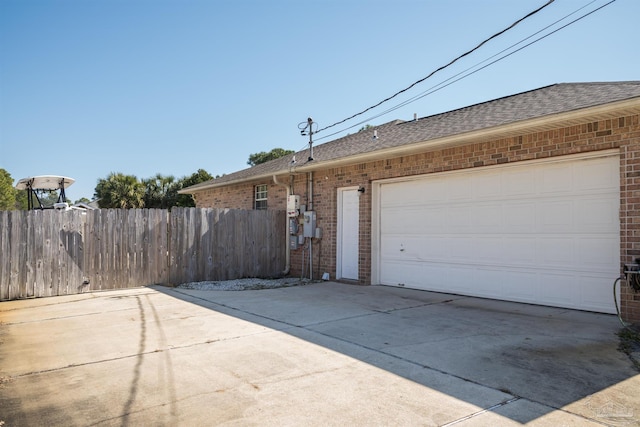 view of property exterior featuring roof with shingles, concrete driveway, fence, and brick siding