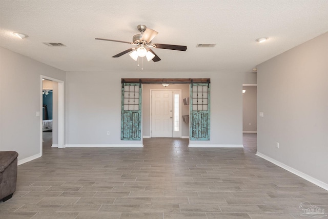 unfurnished living room with visible vents, light wood-style flooring, a ceiling fan, and a barn door