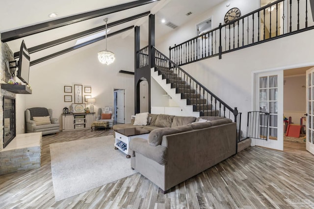 living room with french doors, a stone fireplace, high vaulted ceiling, light hardwood / wood-style flooring, and beam ceiling