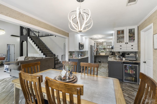 dining room featuring bar, hardwood / wood-style floors, wine cooler, a notable chandelier, and ornamental molding