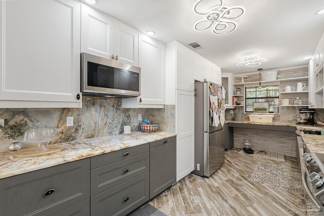 kitchen with appliances with stainless steel finishes, light stone counters, light hardwood / wood-style floors, white cabinets, and decorative backsplash