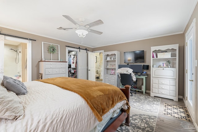 bedroom featuring ensuite bathroom, wood-type flooring, ornamental molding, a spacious closet, and a barn door