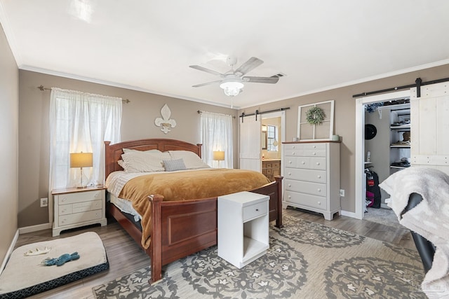 bedroom with crown molding, wood-type flooring, a barn door, a walk in closet, and a closet