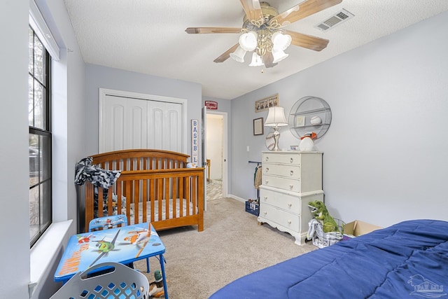 bedroom featuring ceiling fan, light colored carpet, a textured ceiling, and a closet