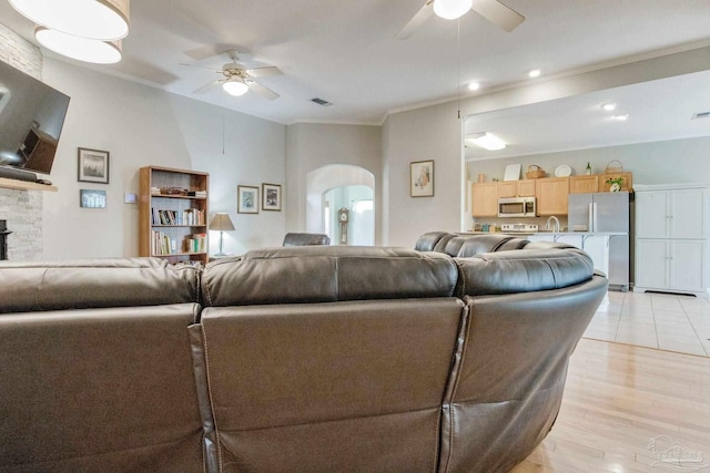 living room featuring light wood-type flooring, crown molding, ceiling fan, and a stone fireplace