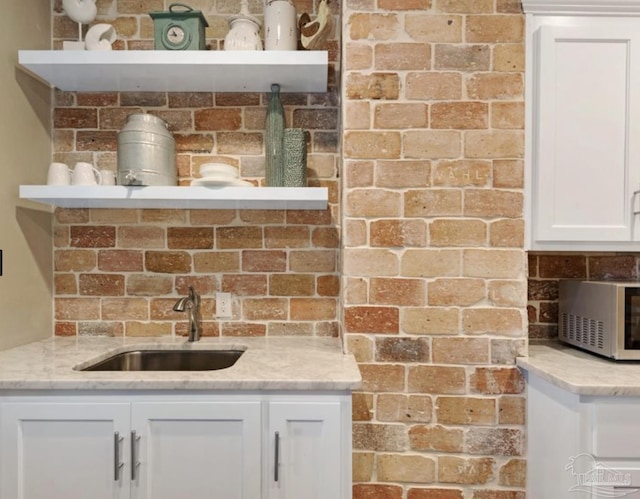 kitchen featuring light stone counters, sink, and white cabinets